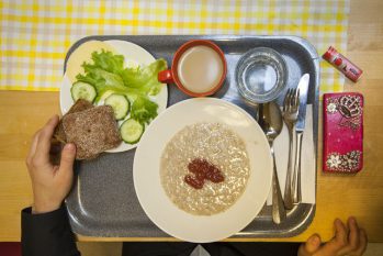 Harmaa tarjotin, jonka päällä puurolautanen, aterimet, vesilasi, kahvikuppi, ja lautanen jossa kurkkua, juustoa, salaattia ja ruisleipää.