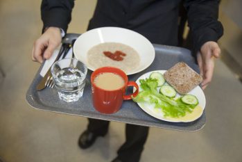 Kuvassa aamiaistarjotin, jonka päällä on puurolautanen, punainen kahvikuppi, leipää, kurkkuviipaleita, salaattia, juustoa ja vesilasi.