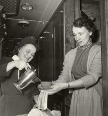 Tarjoilija kaataa kahvia matkustajan pitelemään kahvikuppiin.