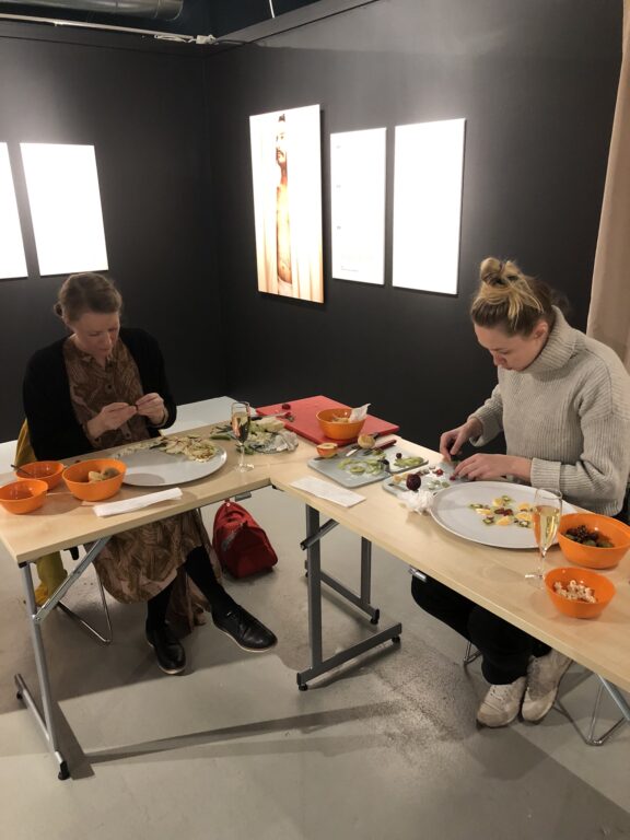 Ruokataidepajan osallistuvat tekevät syötävää taidetta pöytien ääressä.