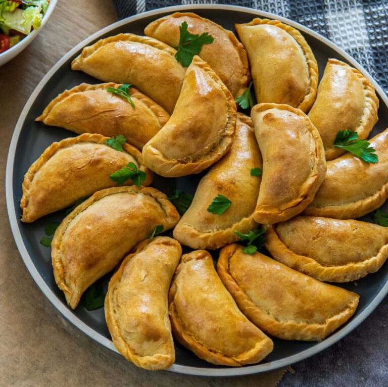 Harmaa lautanen, jolla täytettyjä puolenkuun muotoisia piiraita eli empanadoja.