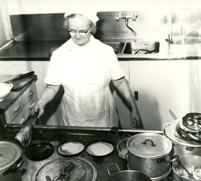 Emäntä paistaa lettuja pannulla lieden ääressä.