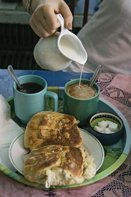 Tarjottimella on kahvia kupeissa, pullaa sekä sokeria.